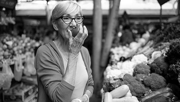 senior woman smelling tomato at market