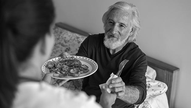caregiver hands dinner to senior man