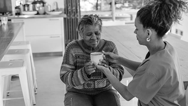 aide helps senior woman hold tea